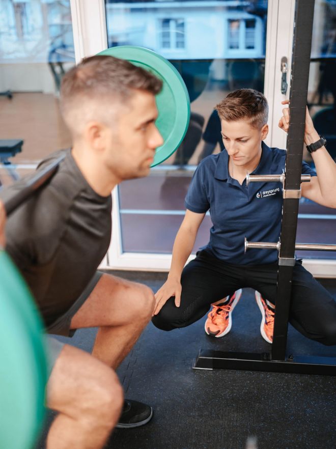 Physiotherapeutin unterstützt Mann bei Gewichtstraining