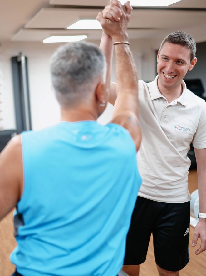 Physiotherapeut unterstützt Patient bei Therapie am Arm.